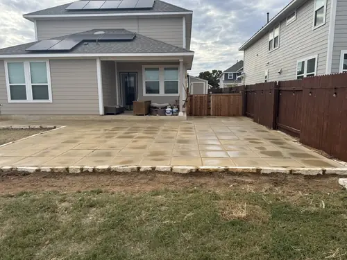 Large square-cut paver patio laid behind a two-storey home and edged in natural stone