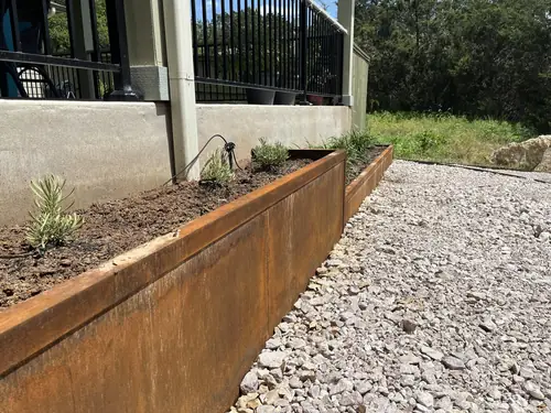 Weathering-steel planter edge holding a new lavender bed against a concrete porch wall