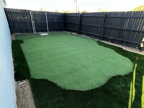 Artificial turf laid into a narrow side yard against a dark stained fence