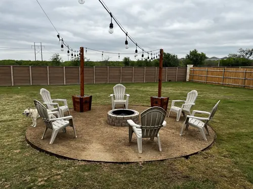 Circular fire-pit patio with a stone ring, string-light posts and Adirondack chairs