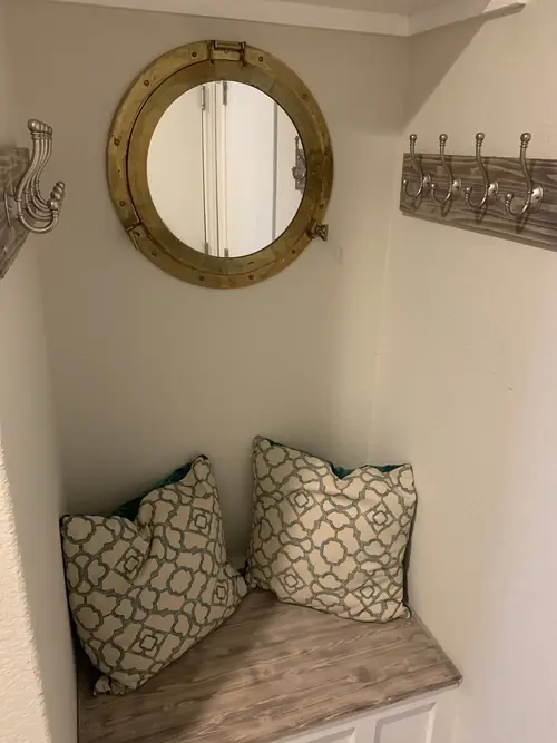 Built-in mudroom bench with a reclaimed-wood top, coat racks and a brass porthole mirror