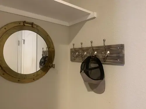 Custom weathered-wood coat rack mounted beside a brass porthole mirror